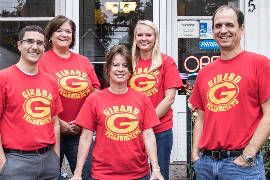 About Our Agency - Team Photo in Matching Red T-shirts in Front of Office Cheering on the Girard Yellowjacket Team